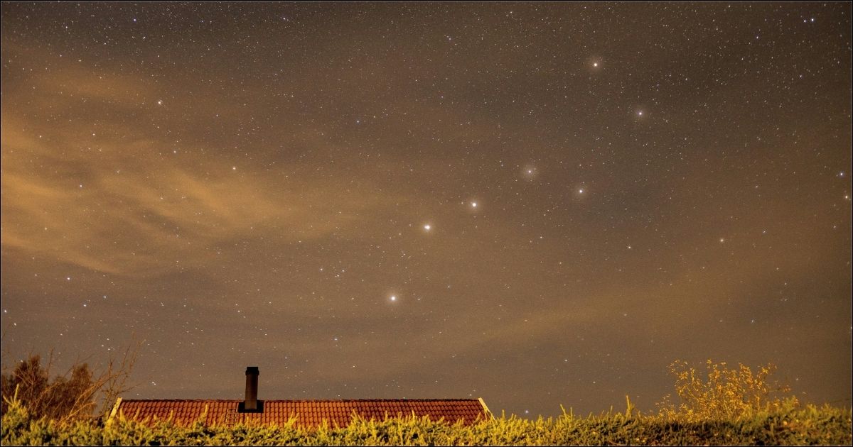 The Big Dipper constellation shines in the evening sky above a farmhouse and grassy landscape.