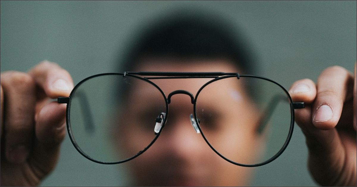 Blurred image of man holding eyeglasses out in clear foreground view representing the importance of Work Clarity.