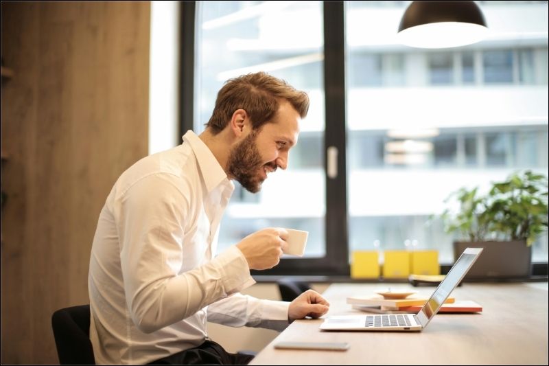 Find Your Rhythm & Groove with MKR Consulting Services Smiling man working on a laptop while holding a cup of tea.